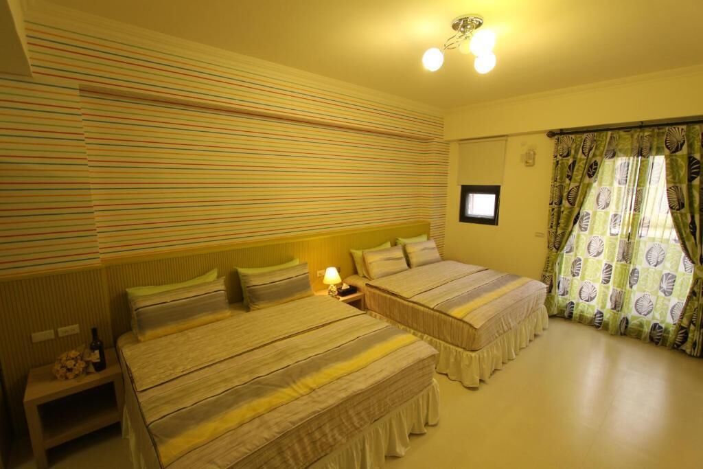 Una habitación con dos camas, una mesita de noche con lámpara, un televisor pequeño y una ventana con cortinas.