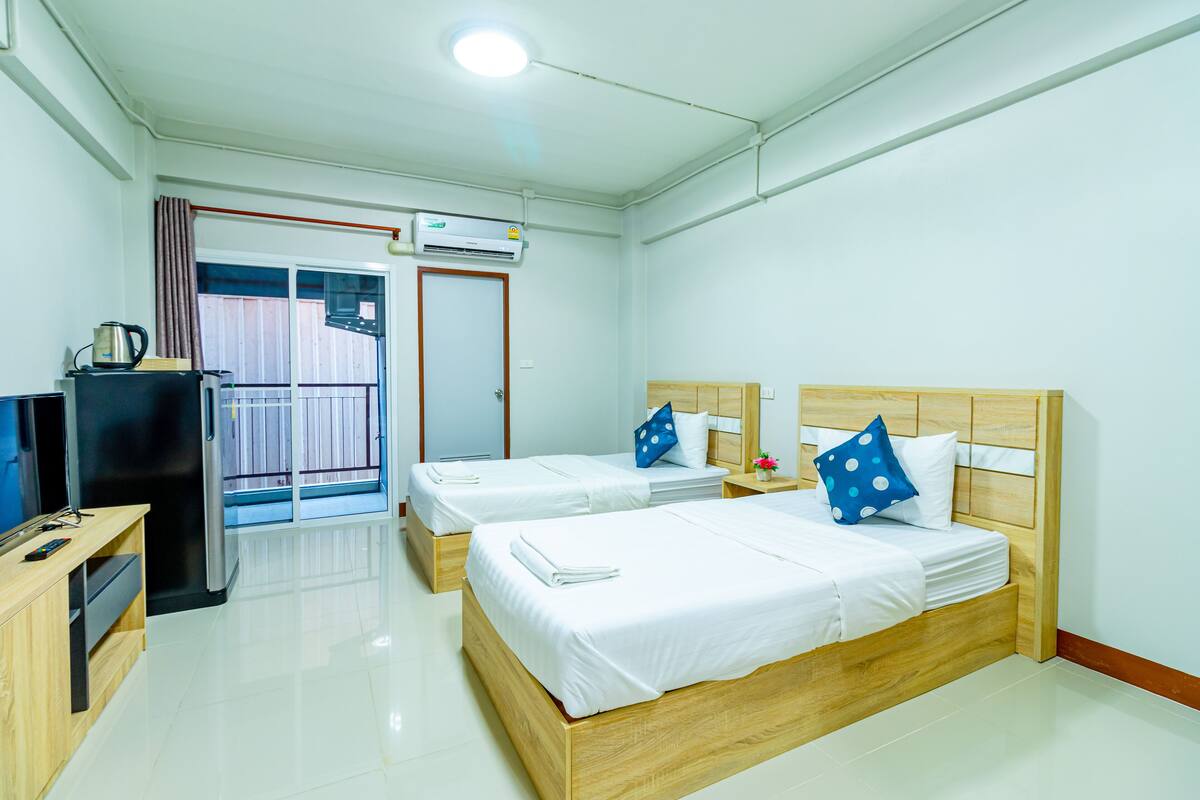 A hotel room with two beds, a TV, a desk, and a window with curtains.