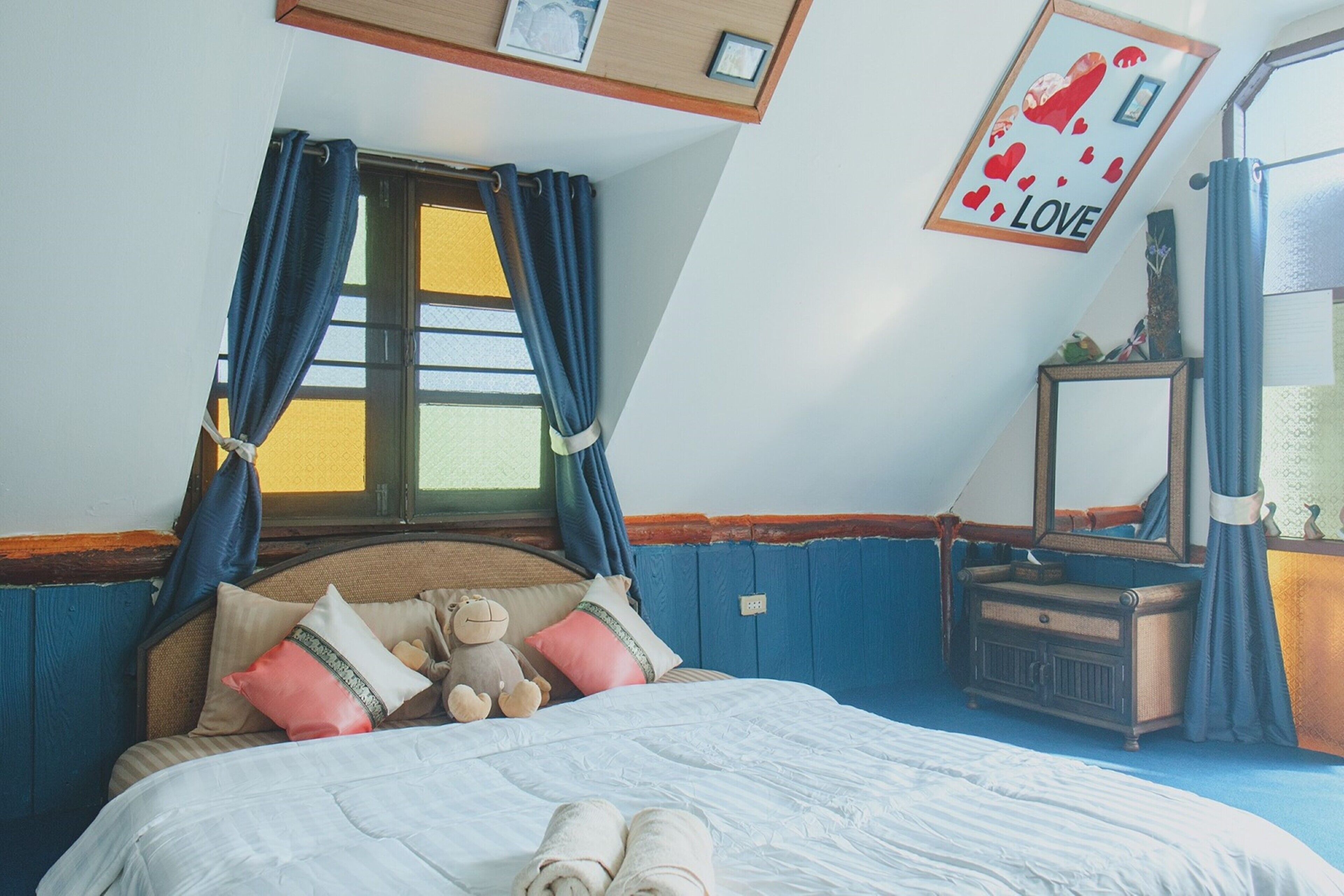 A bedroom with a bed, pillows, a teddy bear, a dresser, and a mirror.
