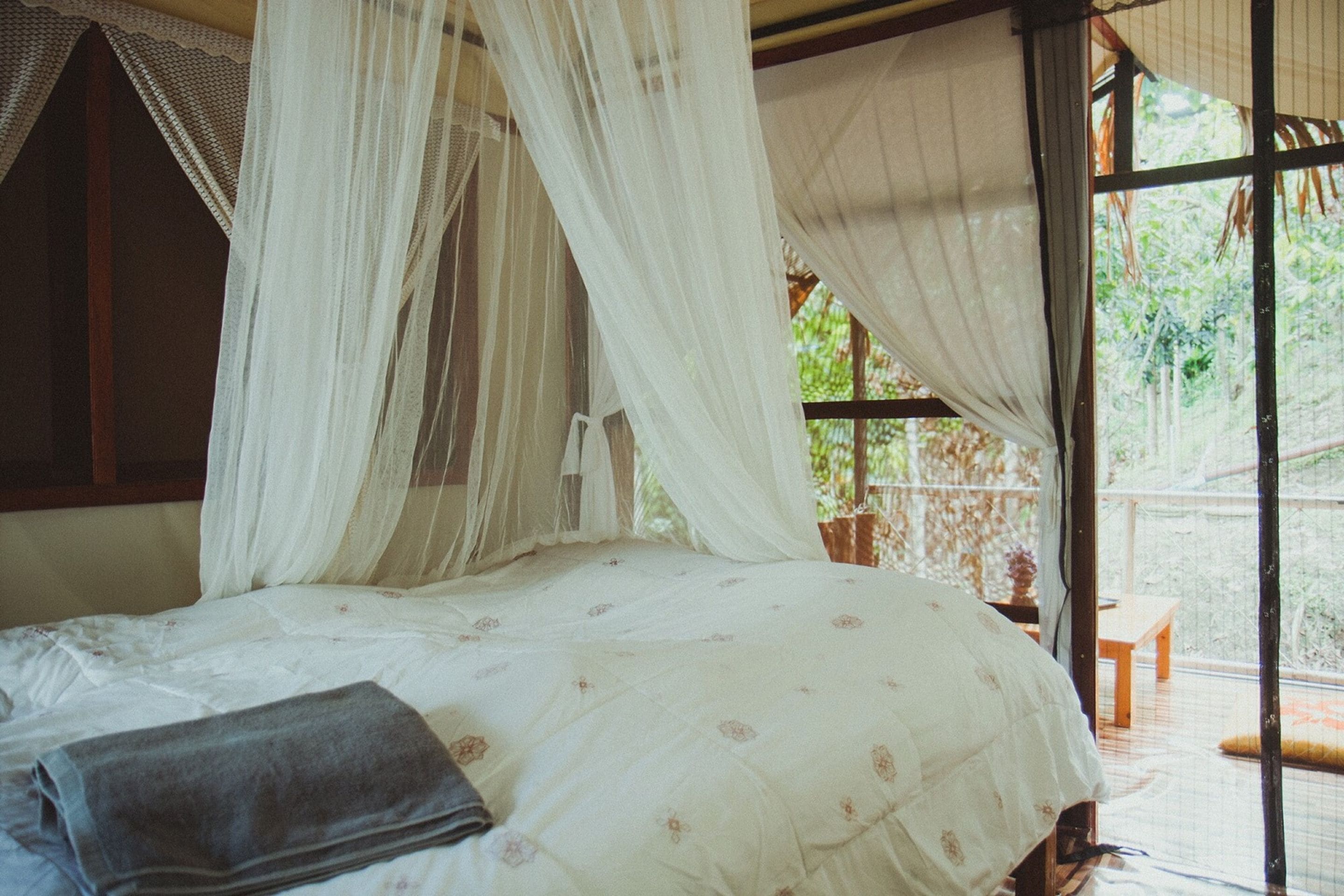 Una cama con dosel, una mesita y vistas al follaje exterior.