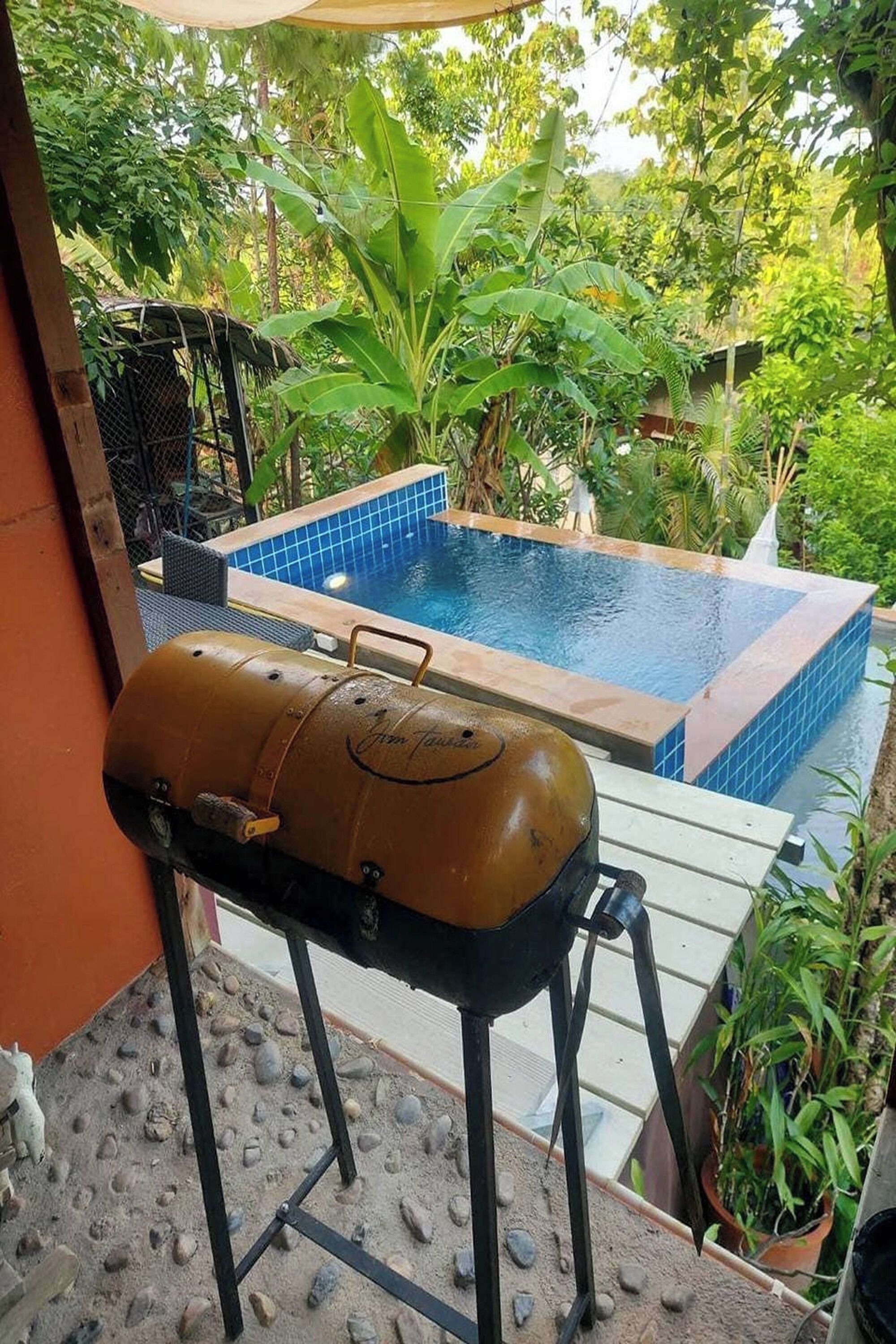 A barbecue grill on a patio with a pool in the background.