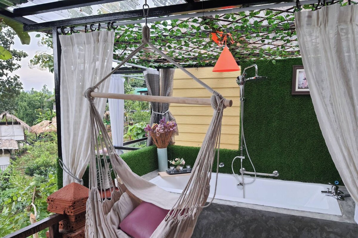 A hammock chair with a cushion, a bathtub, and a hanging orange lantern.