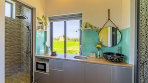 A modern bathroom with a shower, a sink, a mirror, and a window offering a view of a green landscape. - Lua House (Da Nang)