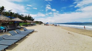A beach with sun loungers and umbrellas, a clear sky, and the ocean in the background. - Lua House (Da Nang)