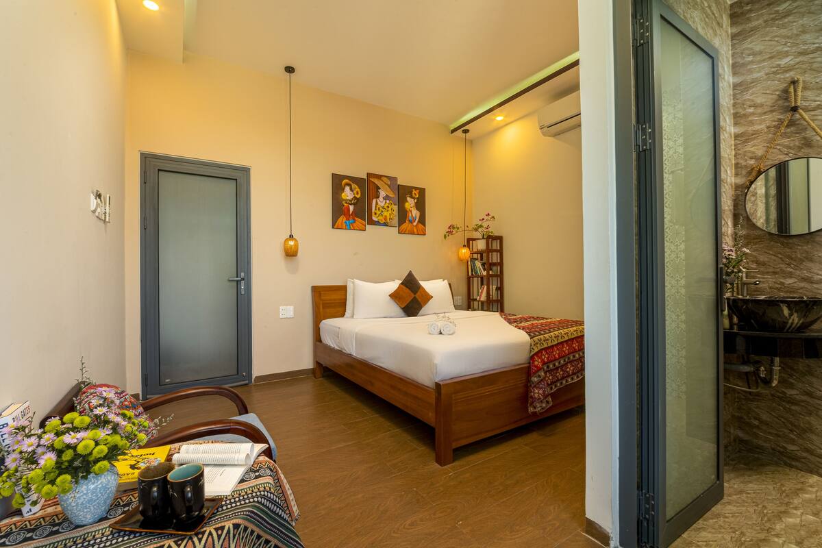 A bedroom with a wooden bed, a desk with a vase of flowers, and a bathroom with a marble wall and a round mirror.