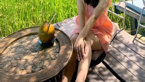 A person sitting on a wooden deck with a woven table beside them, overlooking a lush green field. - Lua House (Da Nang)
