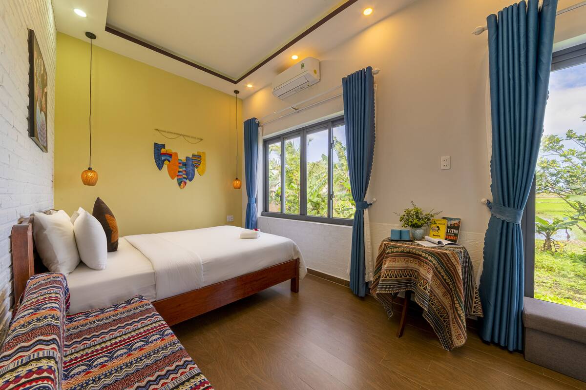 A room with a bed, a small table with a plant, and a window with curtains.
