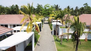 A pathway leading to a row of single-story buildings with sloped roofs, surrounded by palm trees and greenery. - Good Story Village (Ahangama)