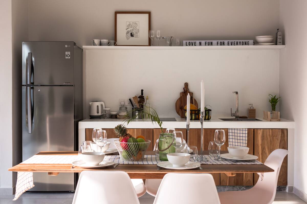A modern kitchen with a stainless steel refrigerator, wooden cabinets, and a dining table set with white chairs.