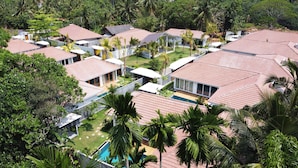 A resort with multiple villas, each with a tiled roof and surrounded by lush greenery and palm trees. - Good Story Village (Ahangama)