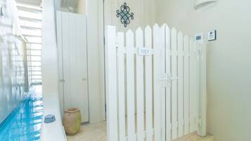 A pool area with a white fence, a door with a 'NAVOS' sign, and a wall-mounted light fixture.