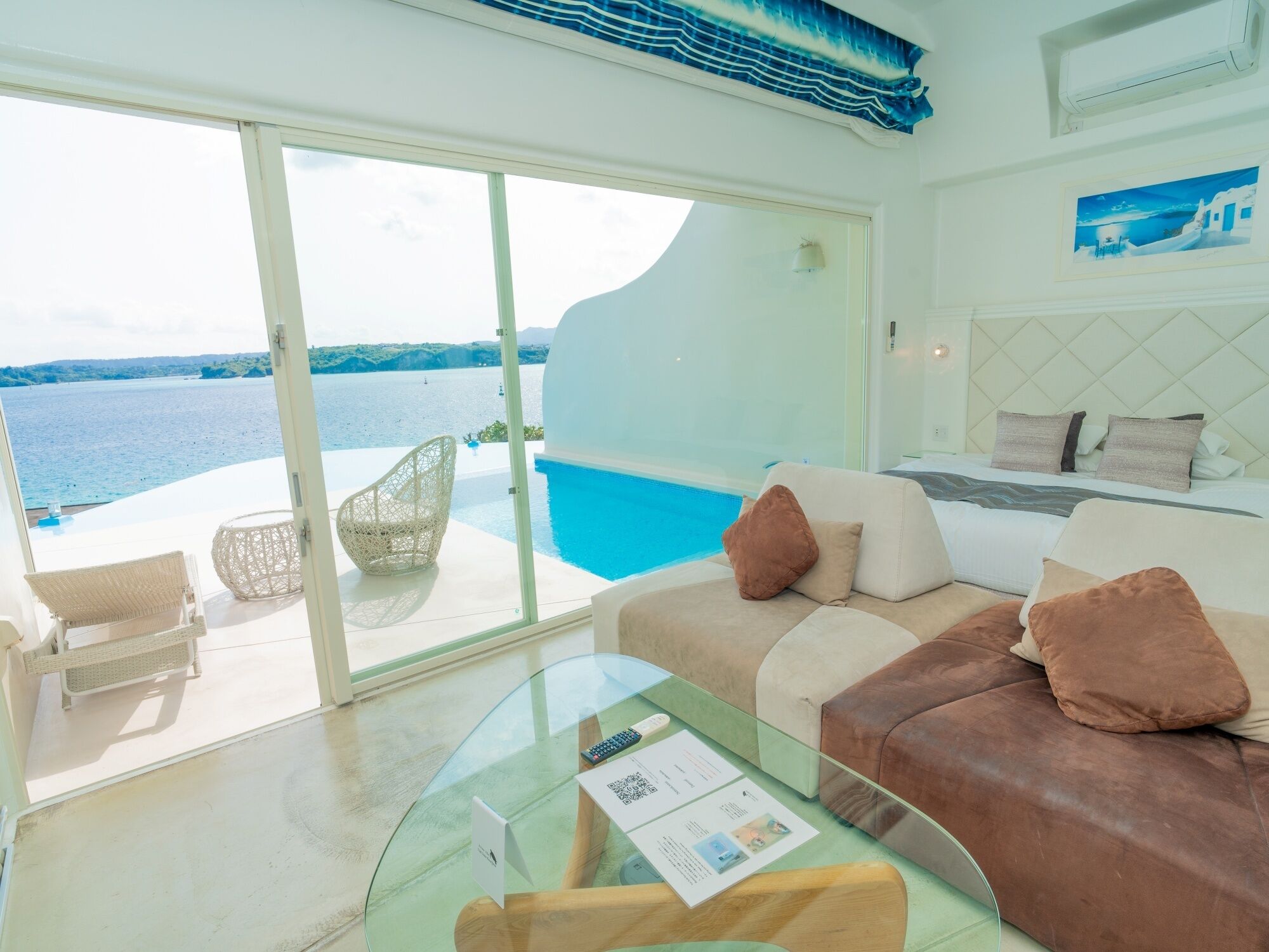 Habitación moderna con mesa de vidrio, sofá y sillón junto a una piscina con vistas al mar.