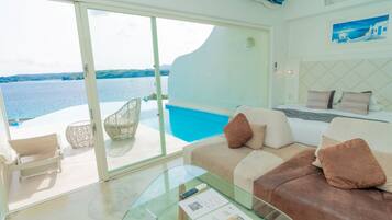 Habitación moderna con mesa de vidrio, sofá y sillón junto a una piscina con vistas al mar.