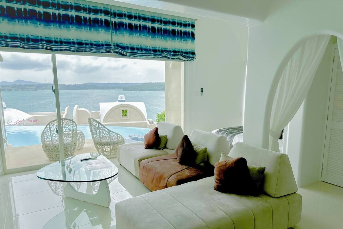 Uma sala de estar moderna com um sofá branco, uma mesa de centro de vidro e vista para o mar.