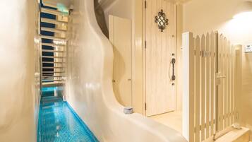 A modern interior with a curved white wall, a blue-tiled pool, a wooden door with a decorative handle, and a white fence.