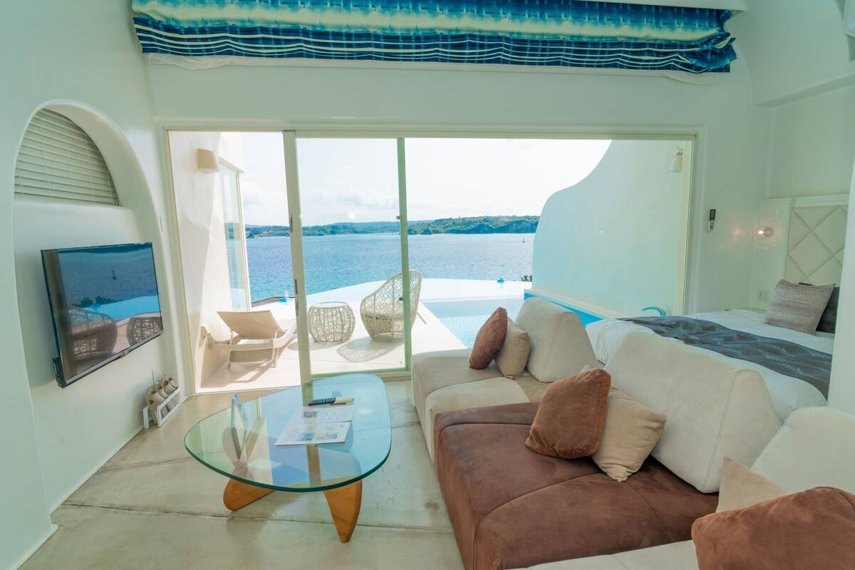 Sala de estar moderna com mesa de vidro, sofá marrom e uma grande janela com vista para a água.