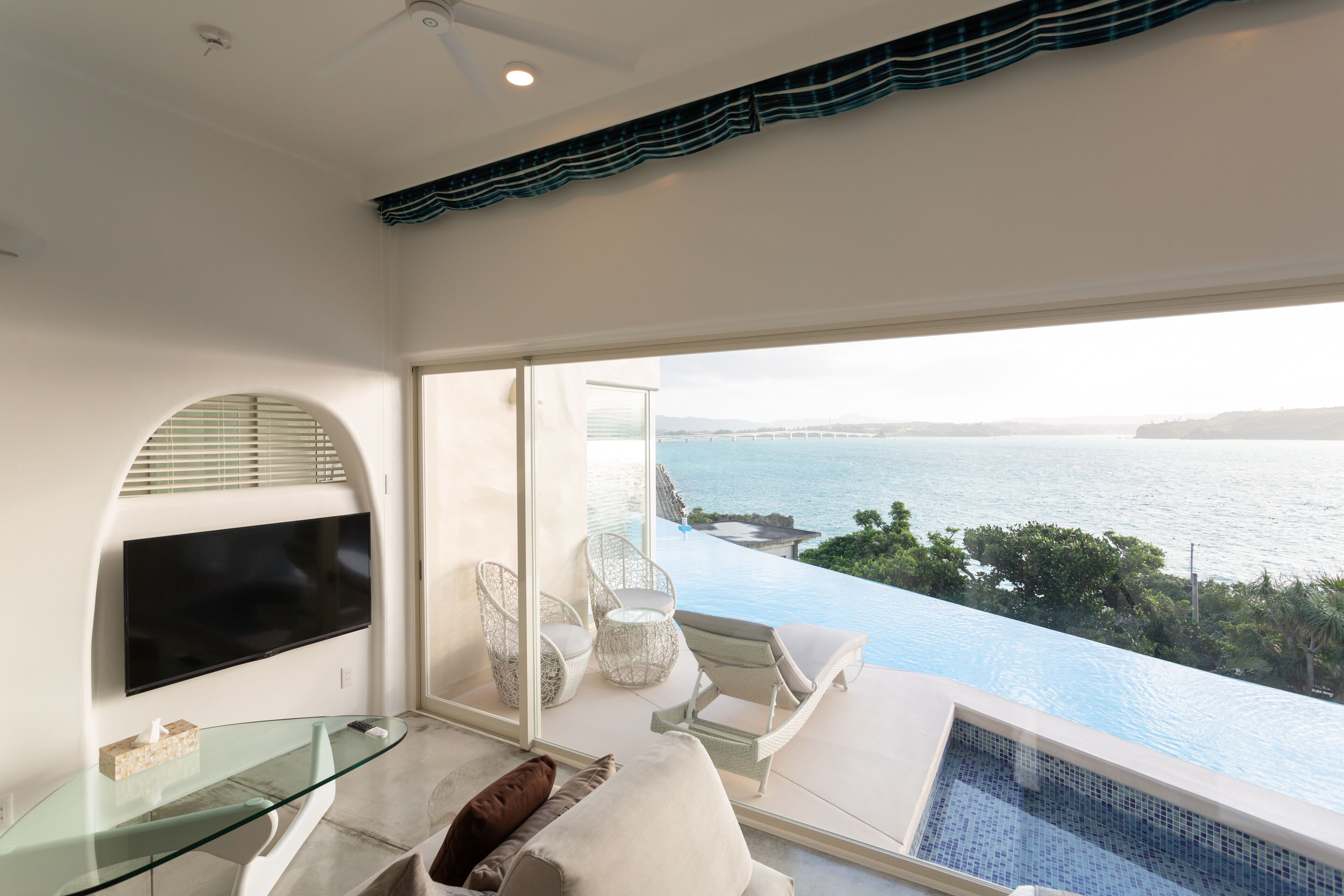 Habitación moderna con mesa de vidrio, televisor de pantalla plana y vista al mar.