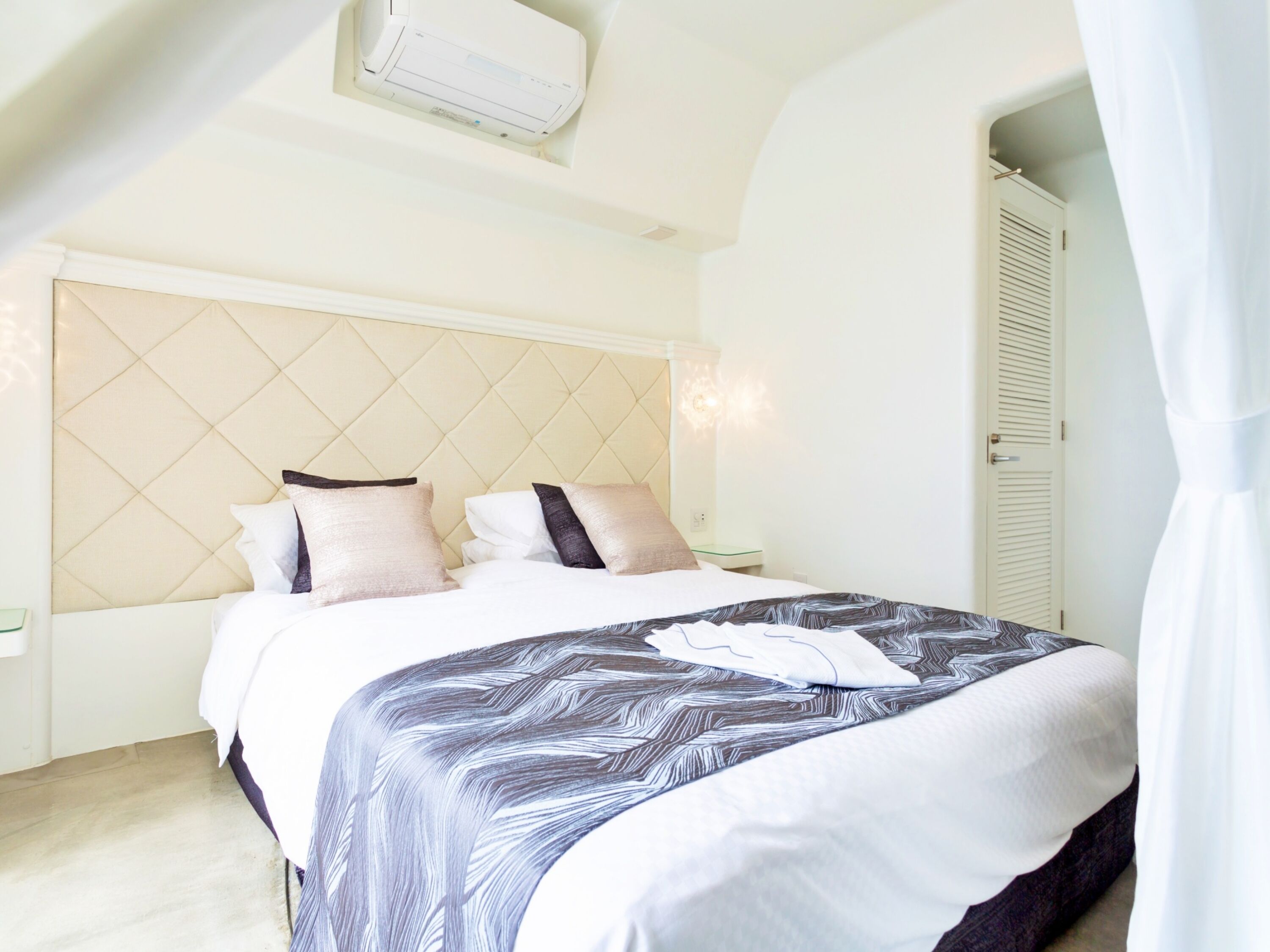 Un dormitorio con cama, mesita de noche, equipo de aire acondicionado y una puerta.