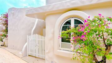 A building with a white facade, a white picket fence, and a window with a view of pink flowers.
