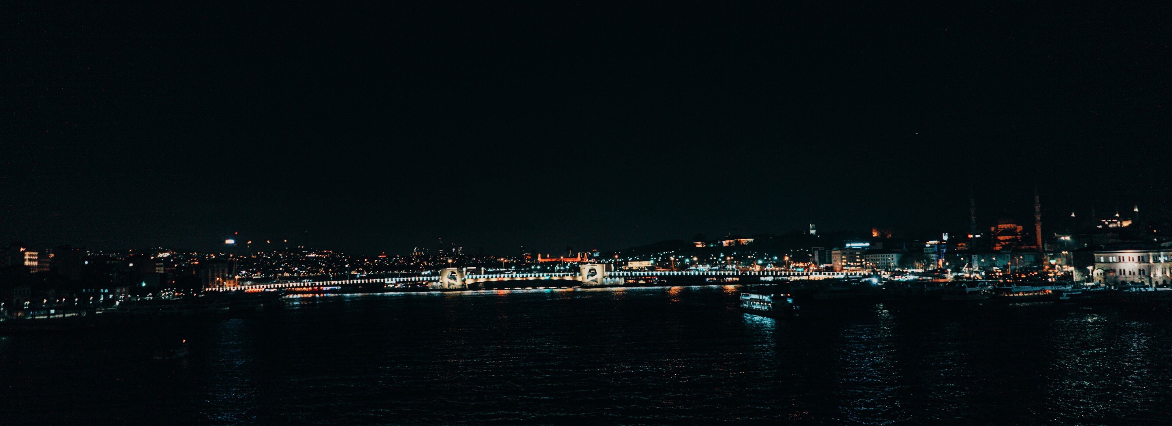 Een verlicht stadsbeeld 's nachts, met een rivier, verlichte bruggen en gebouwen in de verte.