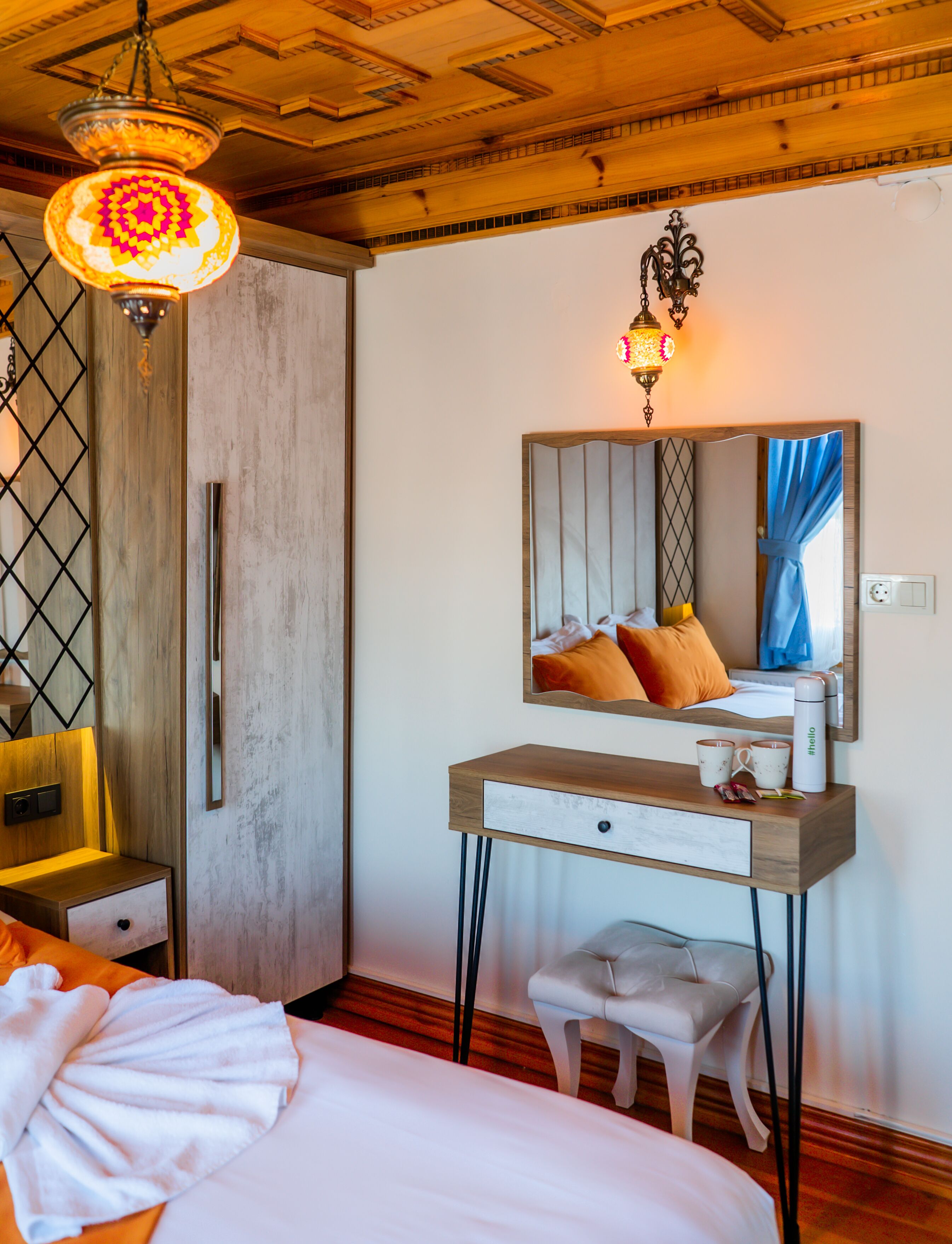 A hotel room with a wooden ceiling, a bed with white linens, a wooden nightstand, a mirror with a wooden frame, and a hanging light fixture.