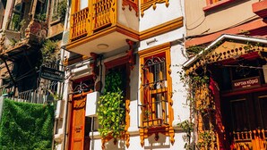 Un immeuble d’angle doté de balcons en bois richement décorés et d’une porte rouge.