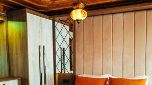 Un lit double avec une literie blanche et orange, une tête de lit en bois et un luminaire suspendu.
