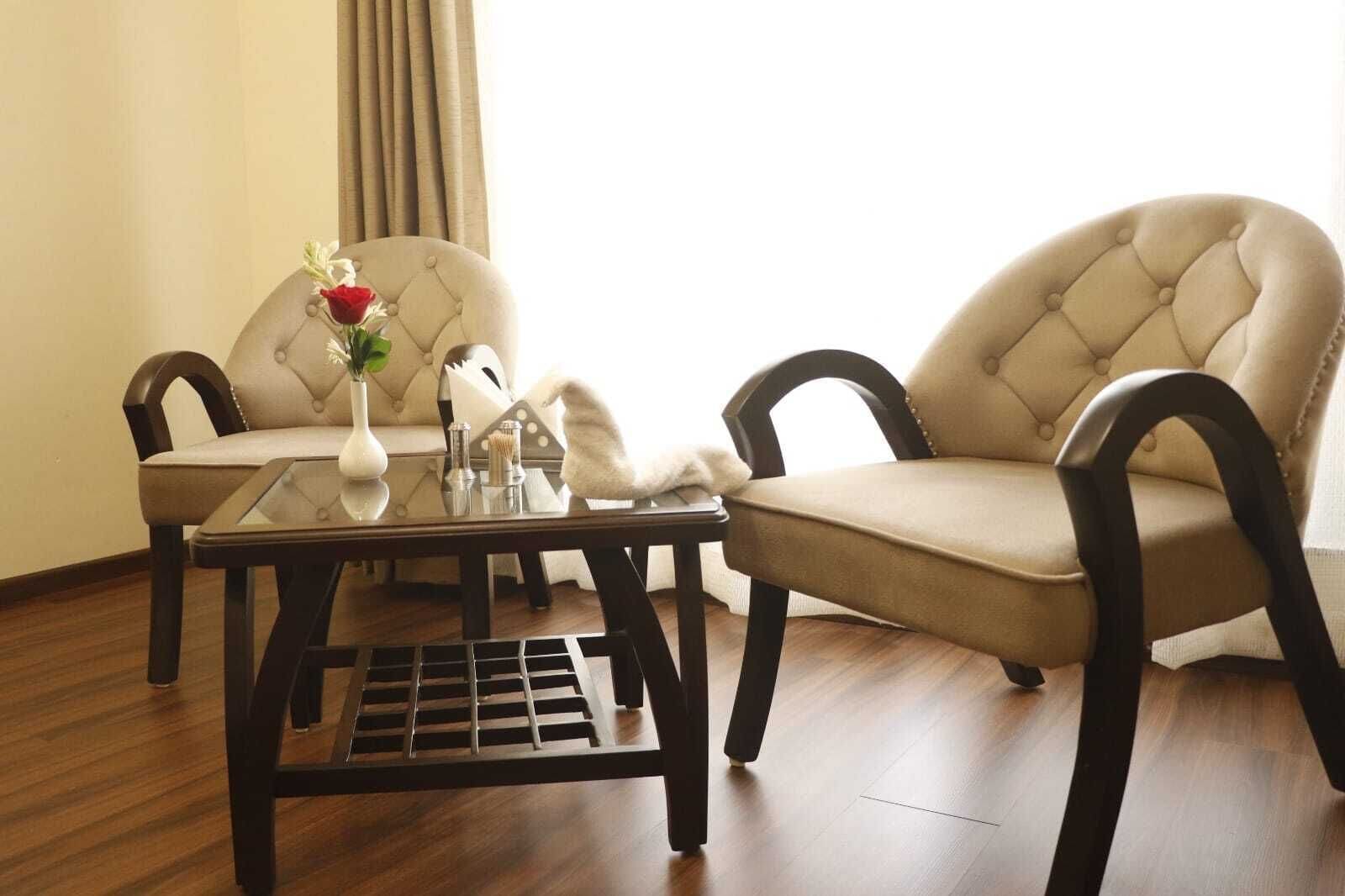 Ein Zimmer mit zwei Polstersesseln, einem Glastisch und einer Blumenvase.