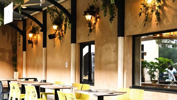 Un restaurante con sillas y mesas amarillas, plantas colgantes y un letrero que dice "MALC".