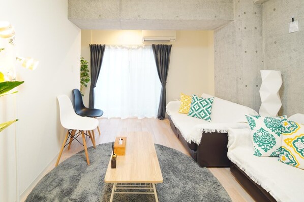 A modern living room with a sofa, two chairs, a coffee table, and a large window with curtains.