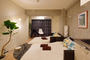 A modern hotel room with a large bed, a sofa, a dining table, and a potted plant.