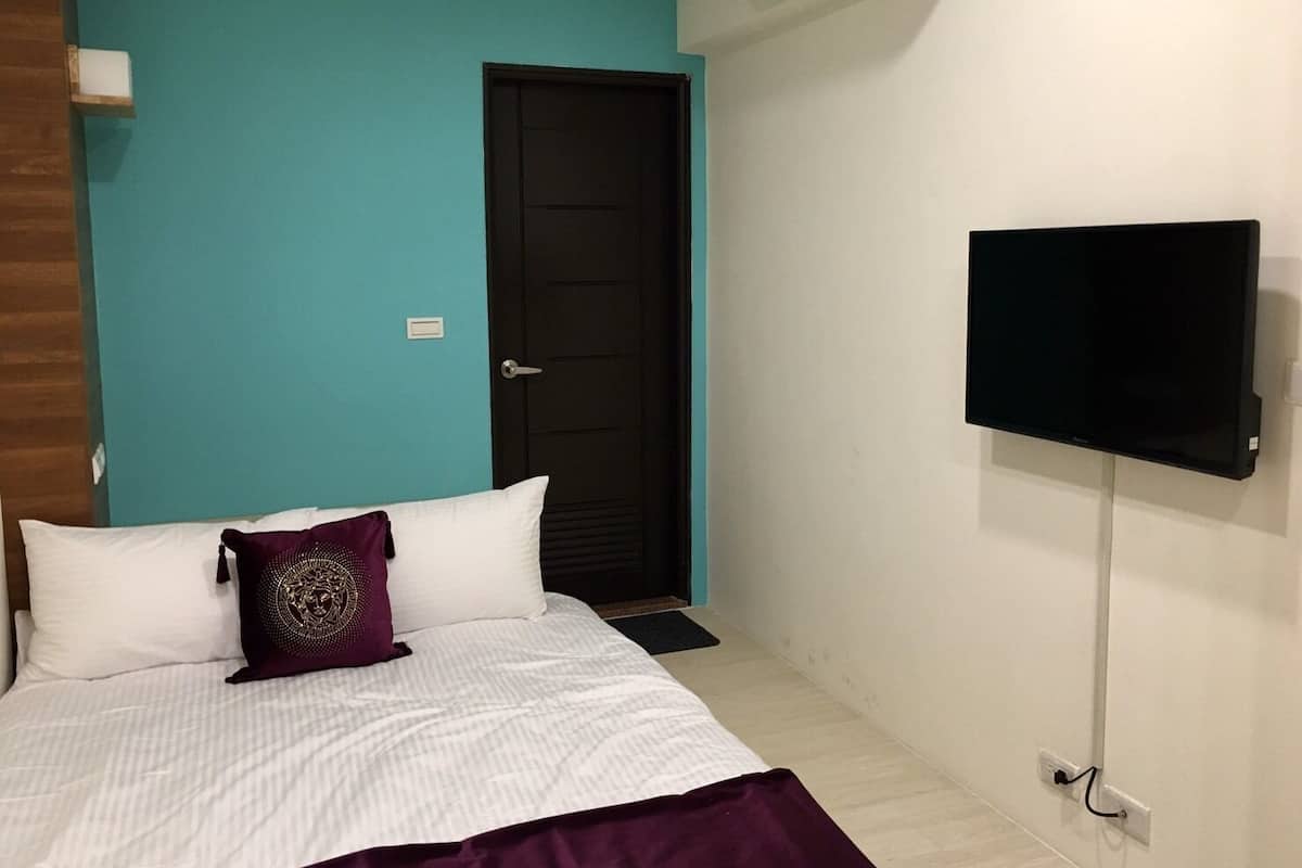 Un dormitorio con cama, televisión montada en la pared y una puerta.