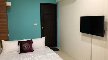 A bedroom with a bed, a television mounted on the wall, and a door.