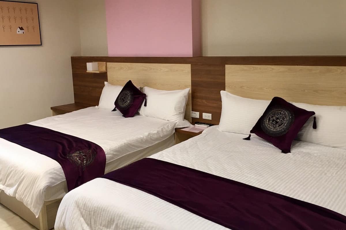 Dos camas dobles con cabeceras de madera, ropa de cama blanca y almohadones morados.