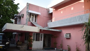 A pink building with a balcony, potted plants, and a parked car. - Grand Inn Guest House (Islamabad)