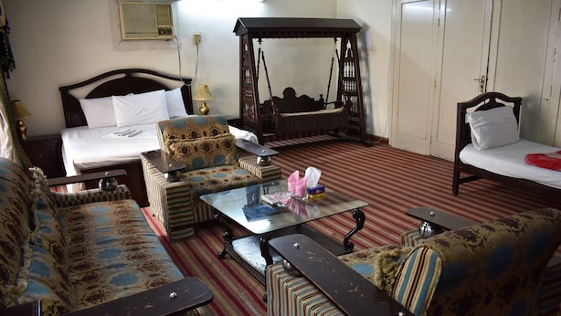 A traditional room with a bed, a sofa, a chair, a glass-top table, and a swing bed. - Grand Inn Guest House (Islamabad)