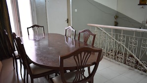 A dining area with a wooden table and chairs, a white railing, and a tiled floor. - Grand Inn Guest House (Islamabad)