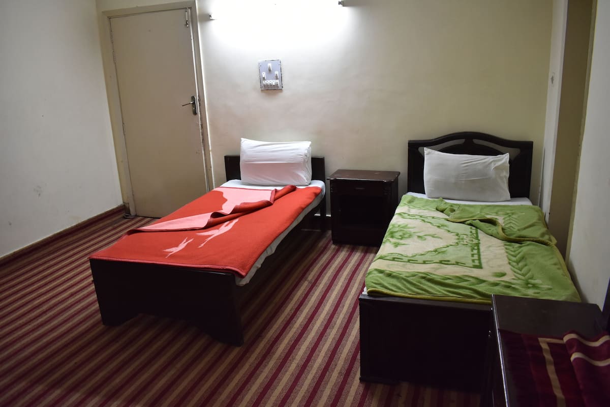 Ein kleines Zimmer mit einem Einzelbett, einem Streifenmuster-Teppich, einem hölzernen Kopfteil und einem Nachttisch.