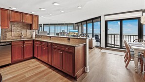 Una cocina amplia con gabinetes de madera y una isla grande, un comedor con mesa y sillas, y un balcón con vistas al océano.