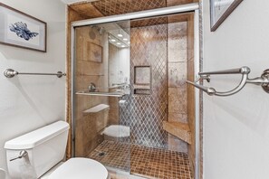 Une salle de bain avec une douche à parois de verre, des toilettes blanches et un tableau encadré au mur.