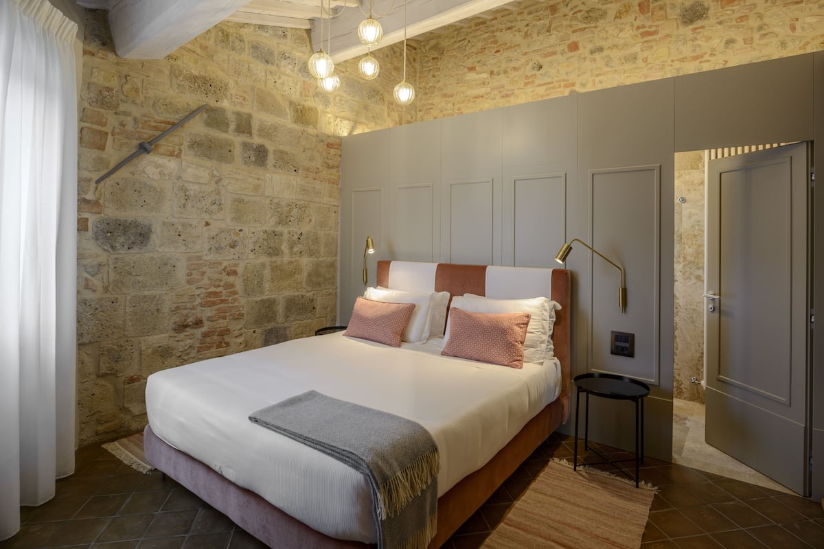 A bedroom with a stone wall, a bed with a wooden headboard, and a modern light fixture.