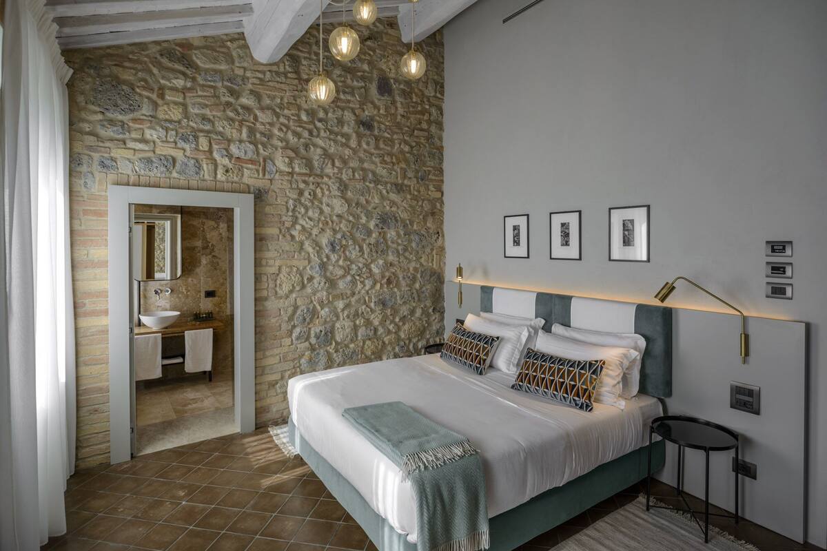 A bedroom with a stone wall, a bed with multiple pillows, a bedside table, and a hanging light fixture.
