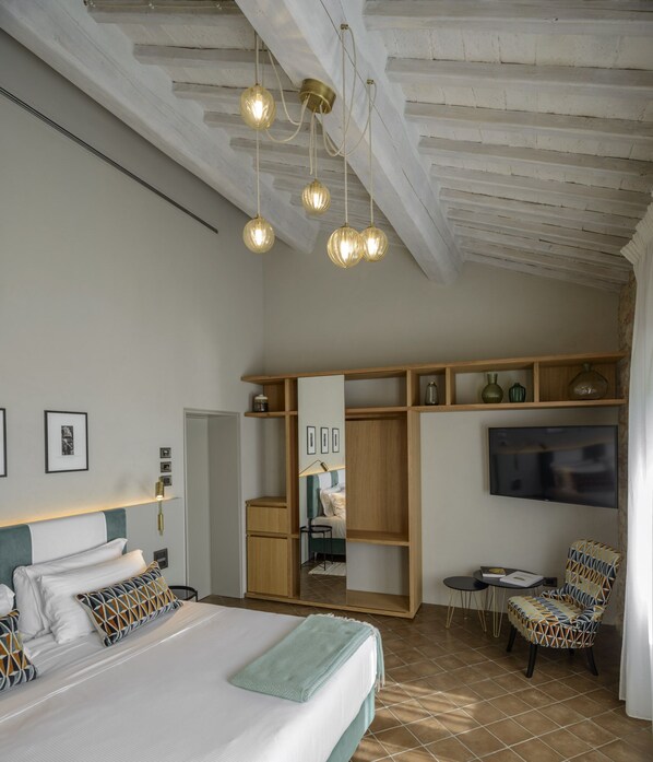 A bedroom with a bed, a chair, a TV, and a shelf with decorative items. - Locanda dei Logi (San Gimignano)