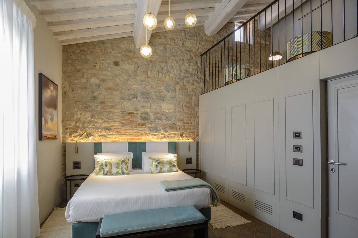 A bedroom with a stone wall, a bed with a bench, a balcony with a railing, and a door with a lock.