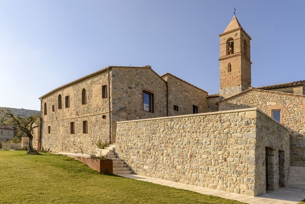 A stone building with a bell tower, a staircase, and a well-maintained lawn. - Locanda dei Logi (San Gimignano)