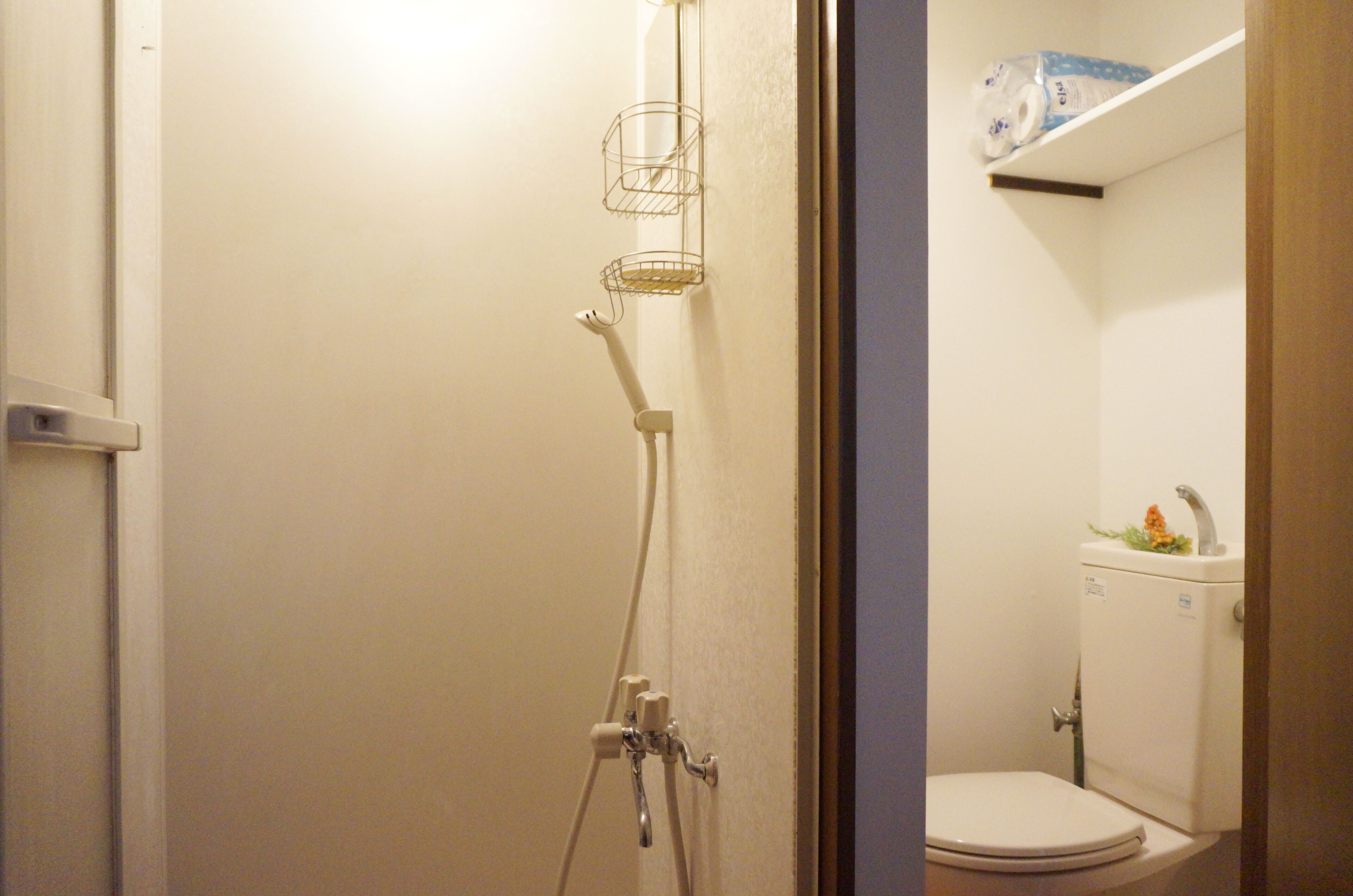 Une salle de bain équipée d’une douche, de toilettes et d’une étagère où sont rangés les articles de toilette.