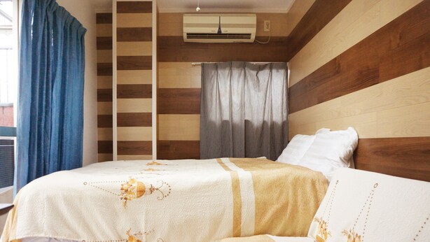 Una camera da letto con un letto, una finestra con tende, un condizionatore d'aria e un pannello di parete in legno.