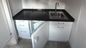 Cocina compacta con armarios blancos, encimera negra y un lavamanos.