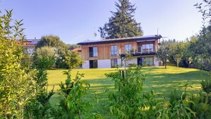 Una casa moderna de dos pisos con un amplio jardín delantero, rodeada de vegetación y árboles.