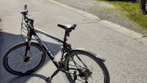 Una bicicleta estacionada en un camino rural, con un pequeño edificio blanco y una estructura de madera al fondo.